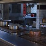 Stainless steel pots on a kitchen counter in a professional restaurant setting.