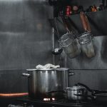 Stainless steel commercial kitchen setup with pots, strainers, and utensils hanging on a rail.